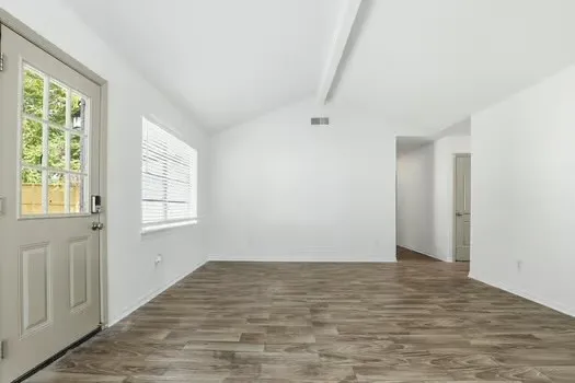 a view of an empty room with wooden floor and a window