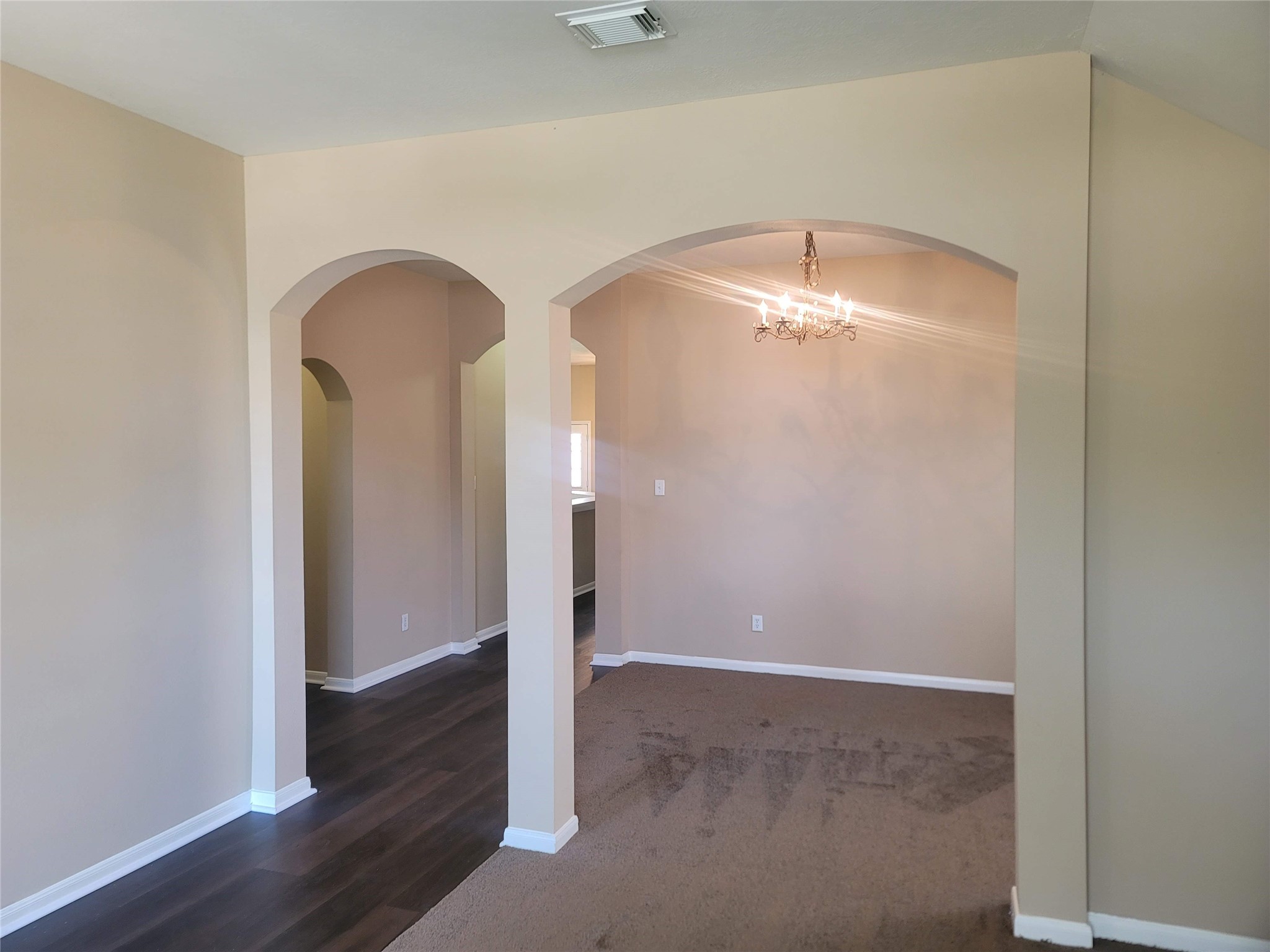 an empty room with wooden floor and way to kitchen