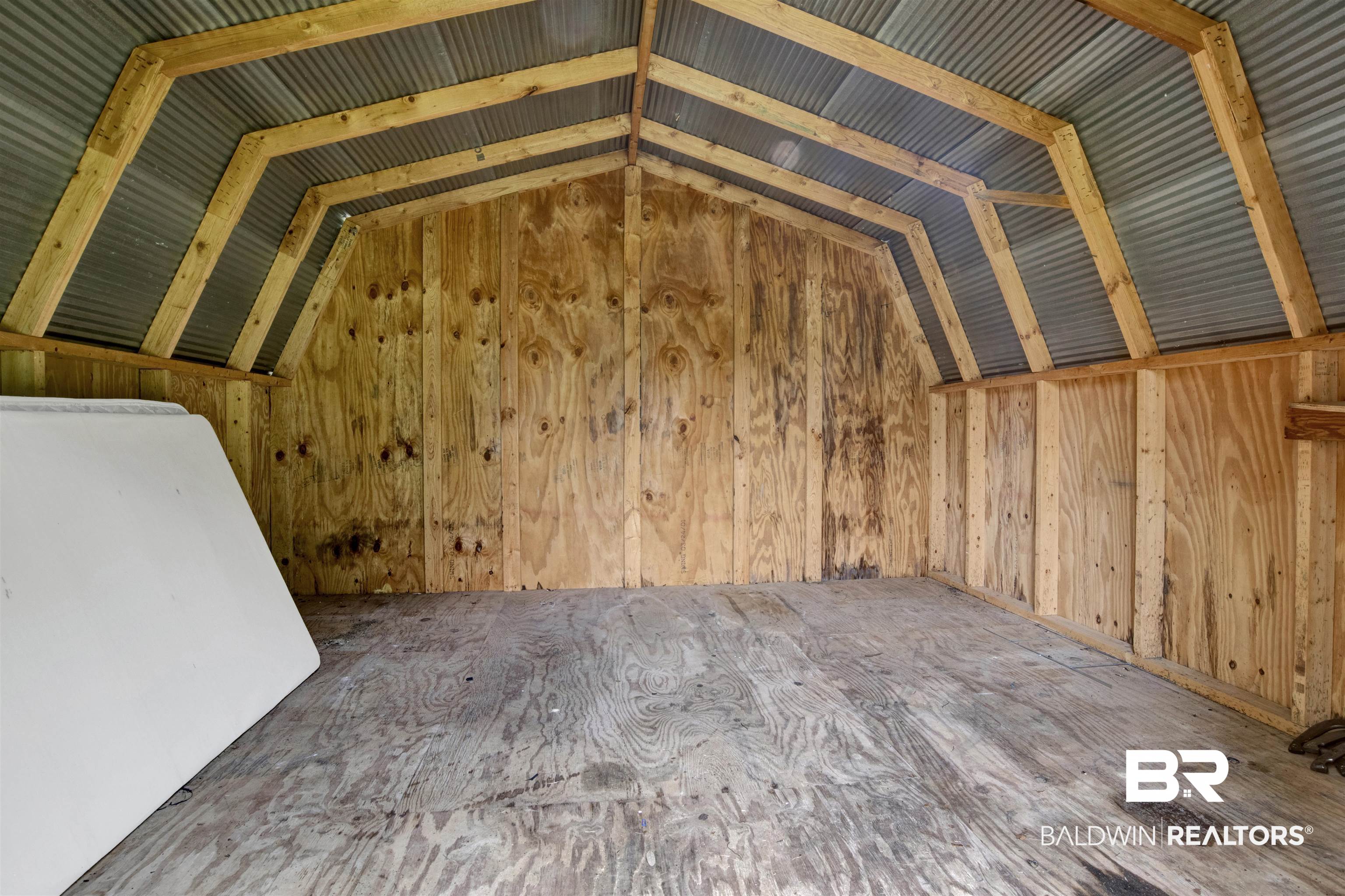 17714 Horseneck Road Bay Minette, AL 36507 - Photo 33 of 36 Spacious shed interior featuring plywood walls and flooring, exposed wood beam framing, and a corrugated metal ceiling
