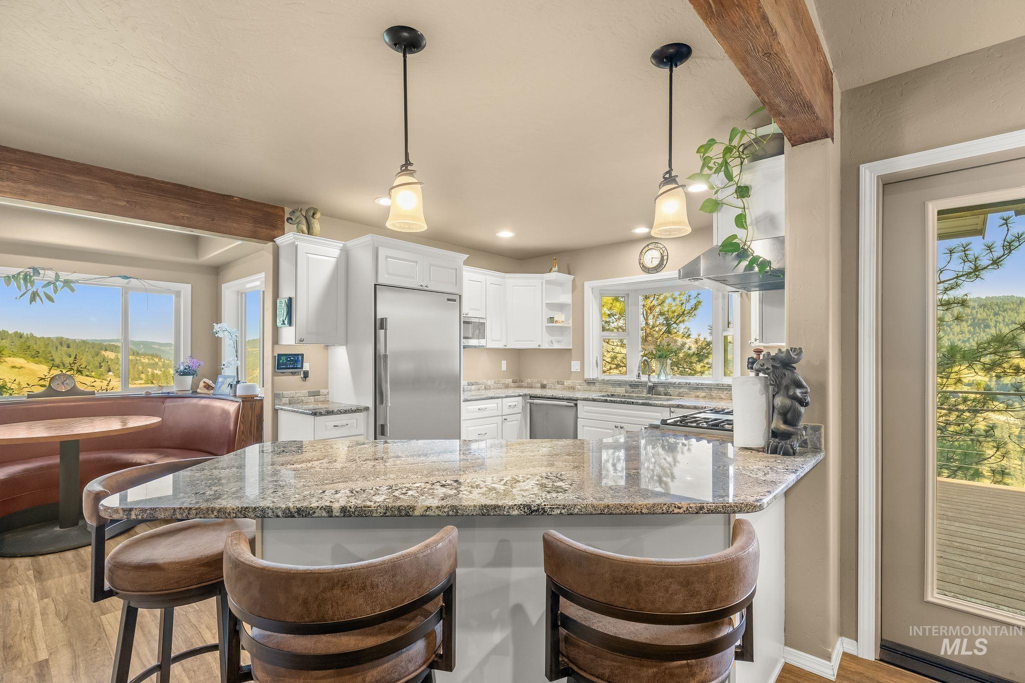 435 River Pointe Lane Lenore, ID 83541 - Photo 8 of 50 Kitchen featuring a granite-topped island, stainless steel appliances, white cabinetry, wood-finish flooring, and exposed ceiling beams