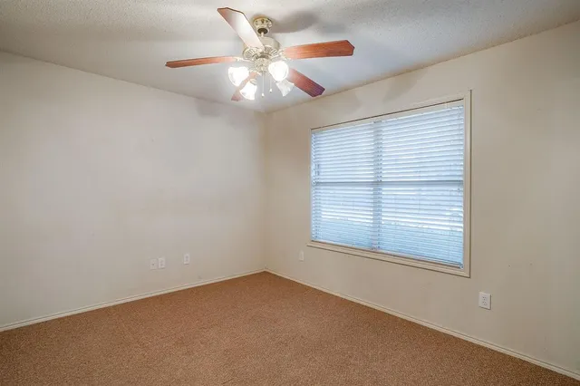 an empty room with chandelier fan and windows