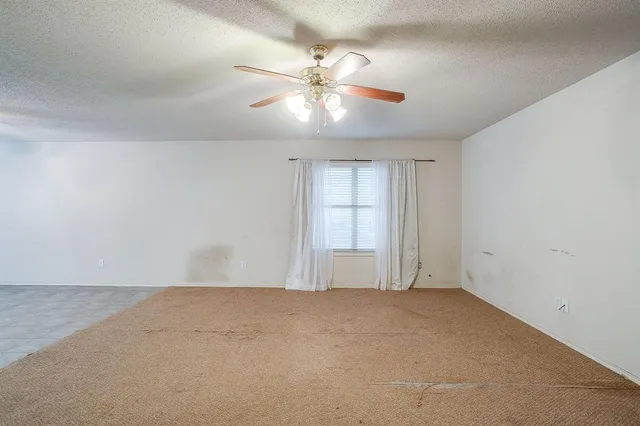 an empty room with chandelier fan and windows