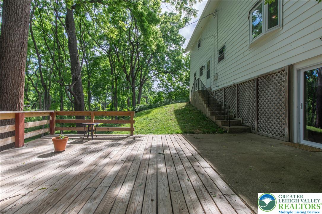 2011 Greenwood Road Allentown, PA 18103 - Photo 44 of 52 A spacious wooden deck transitions to a concrete patio, all against a lush, wooded backdrop.