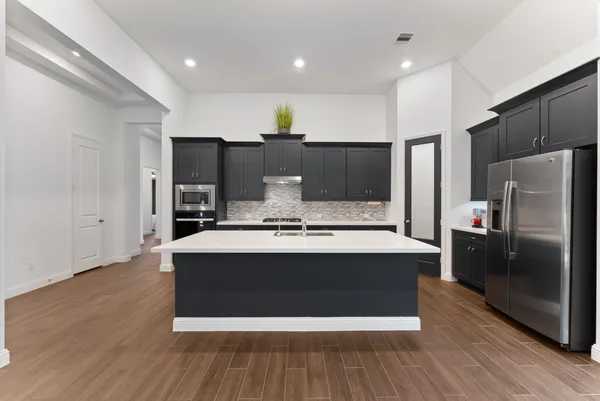 a large kitchen with stainless steel appliances a large counter top and wooden floor