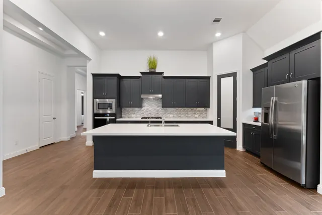 a large kitchen with stainless steel appliances a large counter top and wooden floor