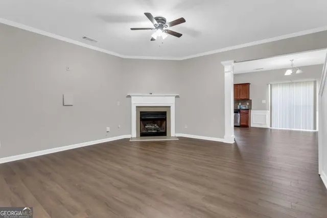 an empty room with wooden floor a ceiling fan a fireplace and windows