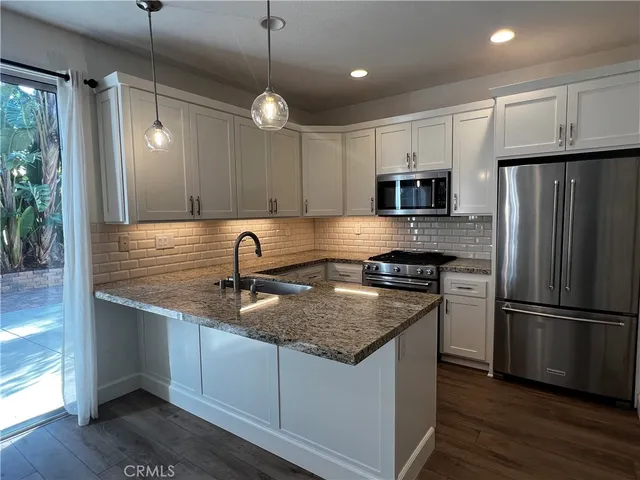 a kitchen with kitchen island granite countertop stainless steel appliances a refrigerator microwave and wooden floor