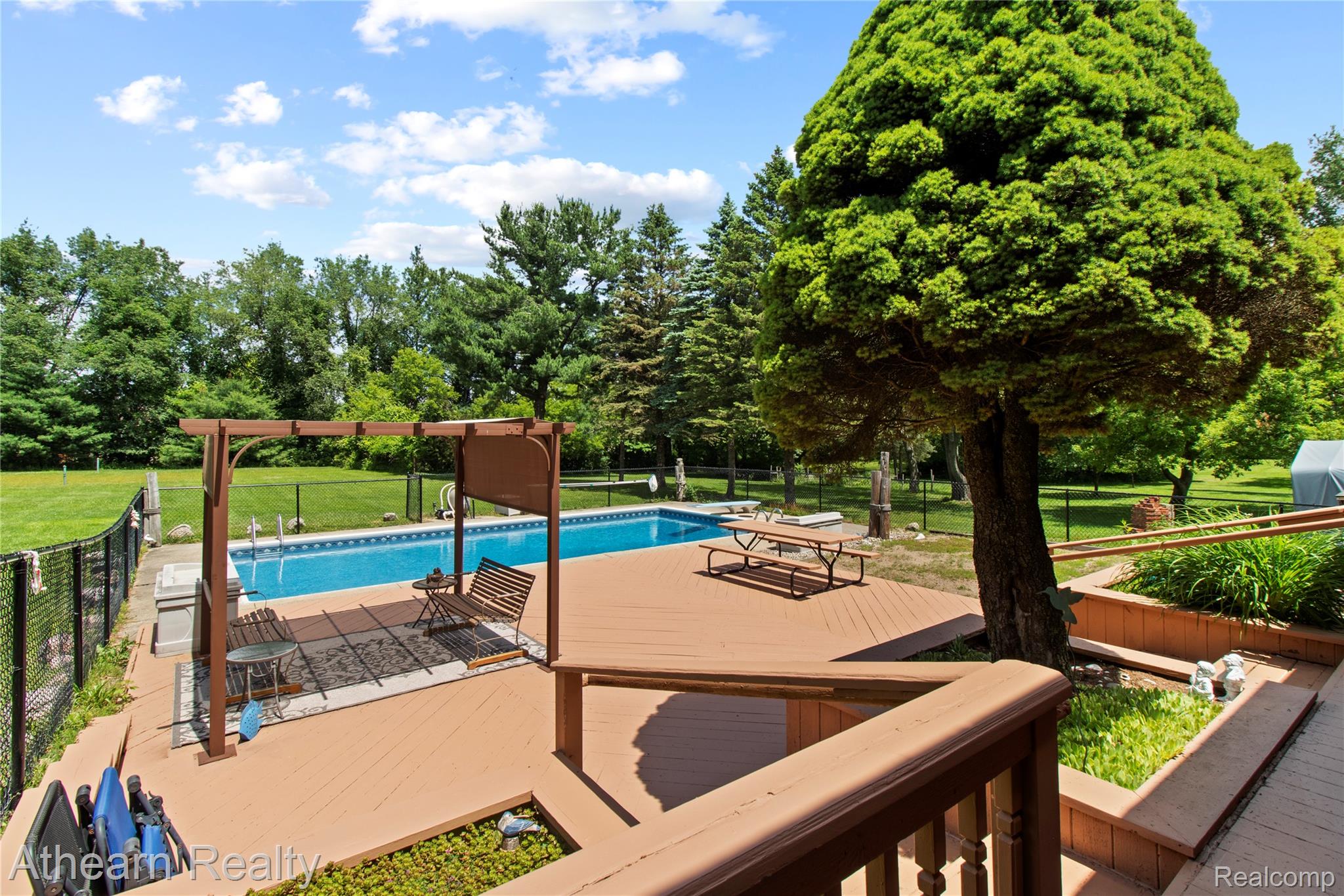 12427 Foley Road Fenton, MI 48430 - Photo 11 of 47 Expansive outdoor living area featuring a large inground pool, spacious wood-finish deck, tiered planters, a wood pergola, and mature trees