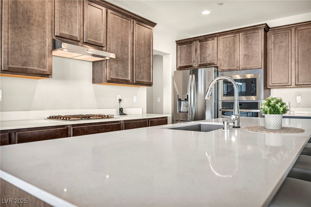 1012 East Sunset Road Henderson, NV 89011 - Photo 30 of 77 Kitchen with stainless steel appliances, light stone countertops, under cabinet range hood, recessed lighting, and dark brown cabinetry