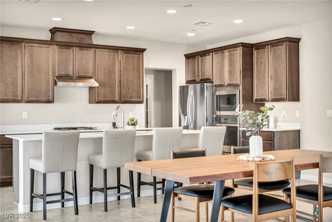 1012 East Sunset Road Henderson, NV 89011 - Photo 47 of 77 Kitchen featuring stainless steel appliances, a kitchen island with sink, a kitchen bar, recessed lighting, and light tile patterned flooring