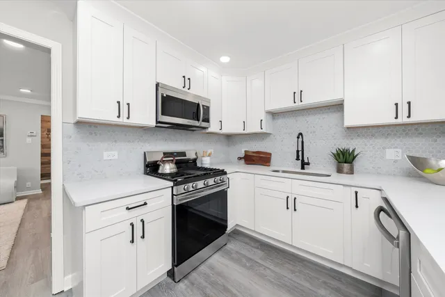 a kitchen with stainless steel appliances granite countertop white cabinets a sink a stove a microwave and wooden cabinets