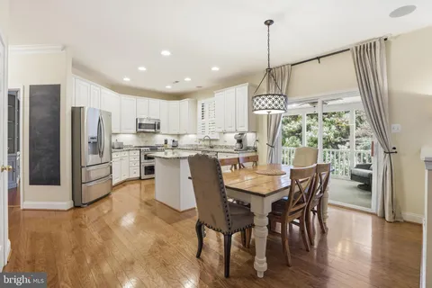 a kitchen with stainless steel appliances kitchen island granite countertop a refrigerator a stove a microwave oven a dining table and chairs with wooden floor