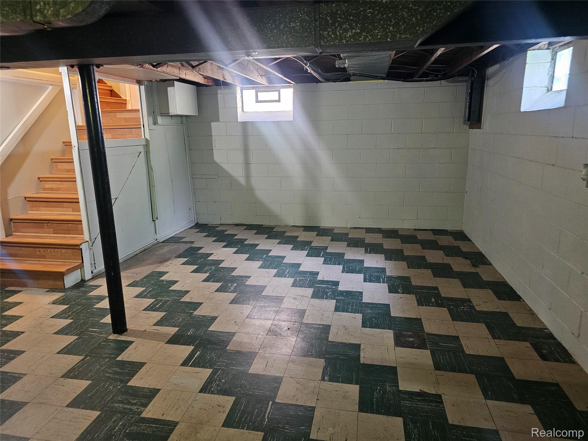 5240 Harvard Road Detroit, MI 48224 - Photo 18 of 18 Spacious lower level featuring a patterned tile floor, exposed ceiling joists, white painted cinder block walls, and natural wood stairs