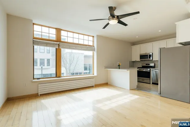 a view of an empty room with a window and kitchen view