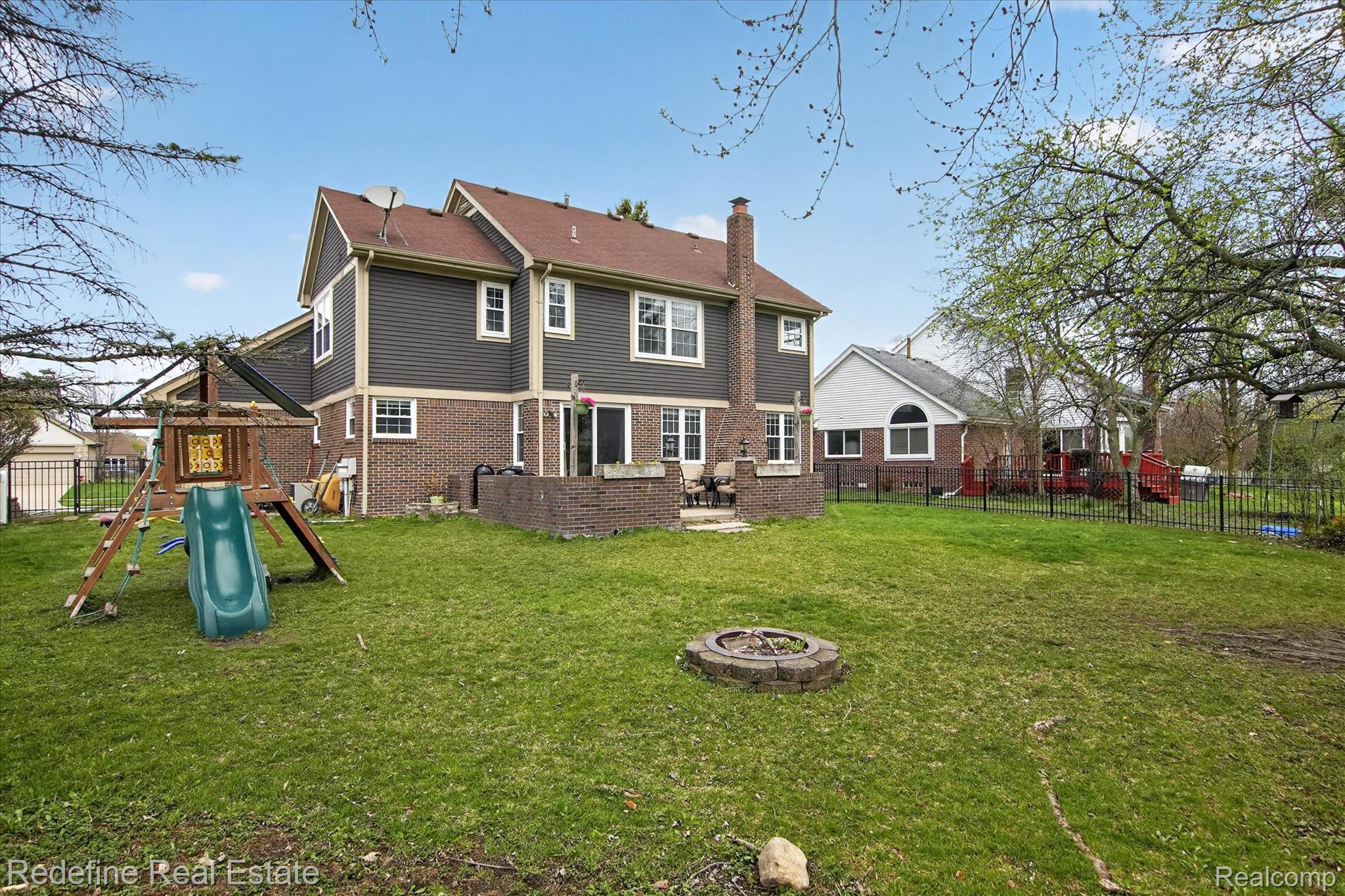 45663 Radnor Road Canton, MI 48187 - Photo 36 of 51 Back of property with a playground, a fenced backyard, a patio area, a fire pit, and a chimney