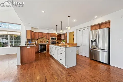 a kitchen with stainless steel appliances granite countertop a refrigerator a stove top oven a sink cabinets and wooden floor