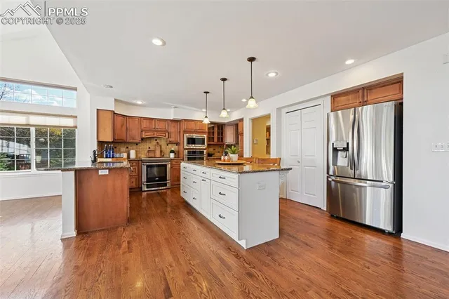 a kitchen with stainless steel appliances granite countertop a refrigerator a stove top oven a sink cabinets and wooden floor