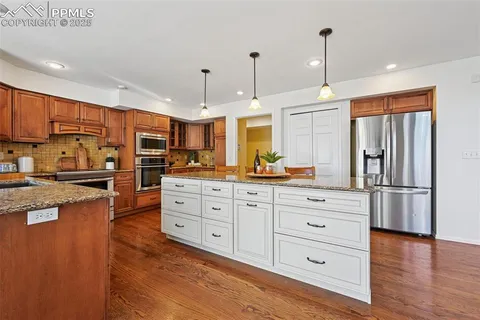 a kitchen with stainless steel appliances kitchen island granite countertop a refrigerator a stove and a wooden floors