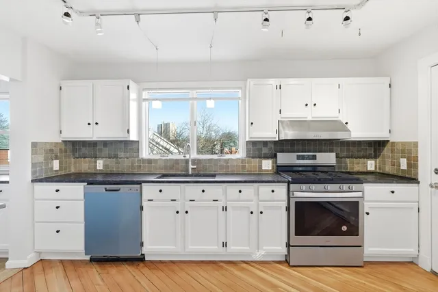 a kitchen with granite countertop a stove a sink and white cabinets