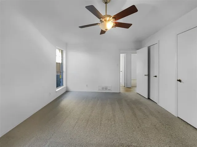 an empty room with chandelier fan and windows