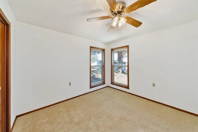 an empty room with chandelier fan and windows