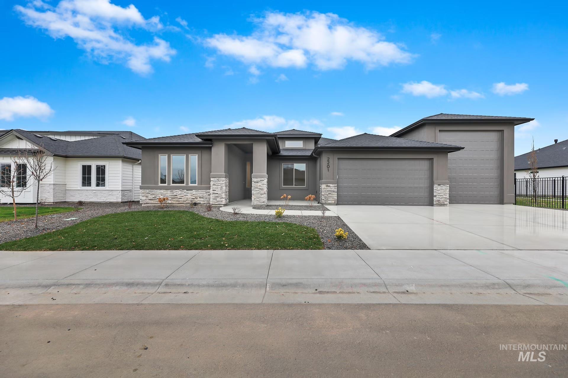 Prairie-style home featuring an attached garage, concrete driveway, stone siding, and stucco siding