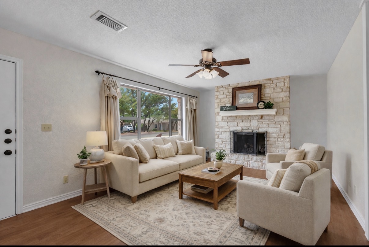 Living room featuring a ceiling fan, a stone fireplace, wood finished floors, and a textured ceiling