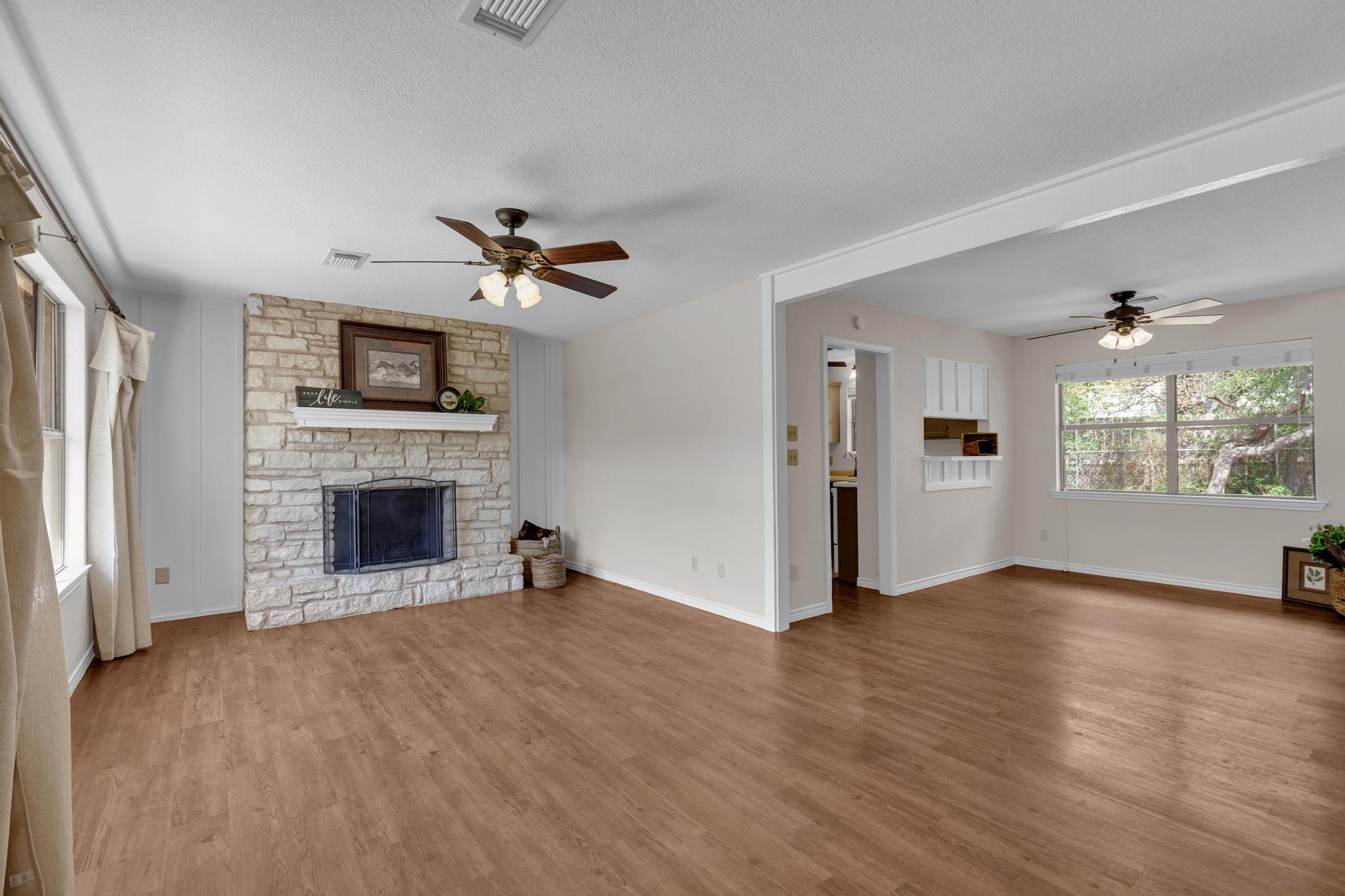 7902 Bar K Ranch Road Lago Vista, TX 78645 - Photo 2 of 35 Unfurnished living room with ceiling fan, a fireplace, a textured ceiling, and wood finished floors