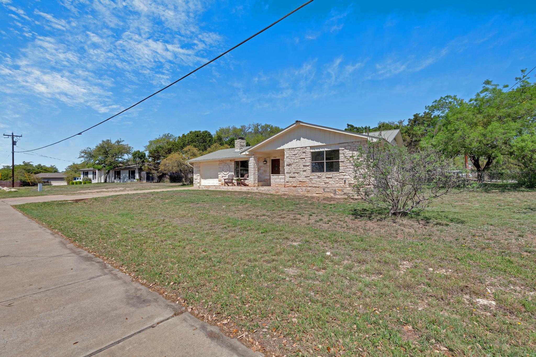 7902 Bar K Ranch Road Lago Vista, TX 78645 - Photo 30 of 35 View of front facade with stone siding, a front lawn, a garage, driveway, and a chimney