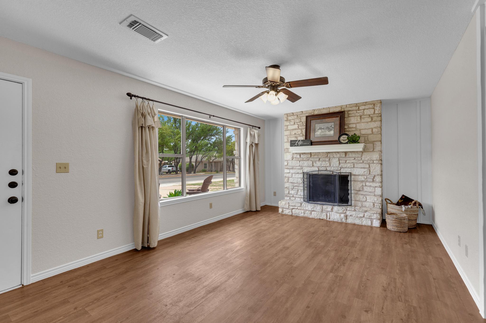 7902 Bar K Ranch Road Lago Vista, TX 78645 - Photo 3 of 35 Unfurnished living room featuring a ceiling fan, wood finished floors, a textured ceiling, and a stone fireplace