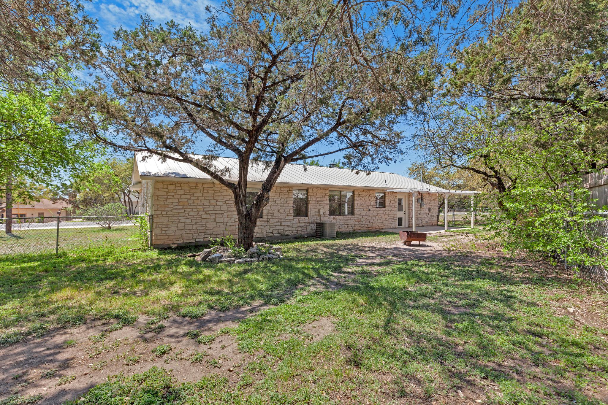 7902 Bar K Ranch Road Lago Vista, TX 78645 - Photo 34 of 35 Back of house featuring a fenced backyard, a patio, an outdoor fire pit, and a metal roof