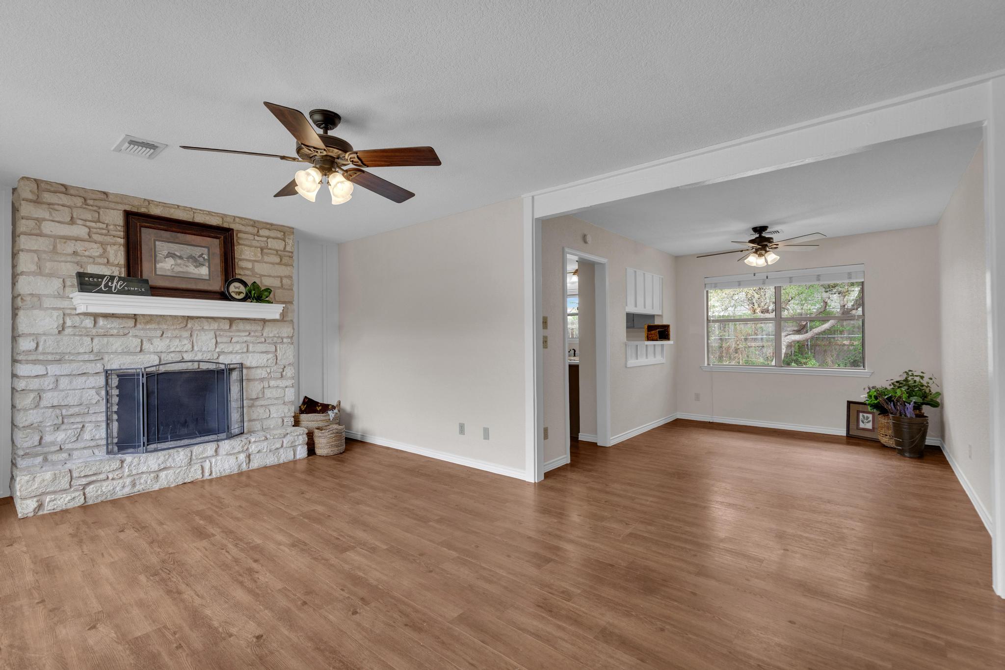7902 Bar K Ranch Road Lago Vista, TX 78645 - Photo 4 of 35 Unfurnished living room with a ceiling fan, a stone fireplace, wood finished floors, and a textured ceiling
