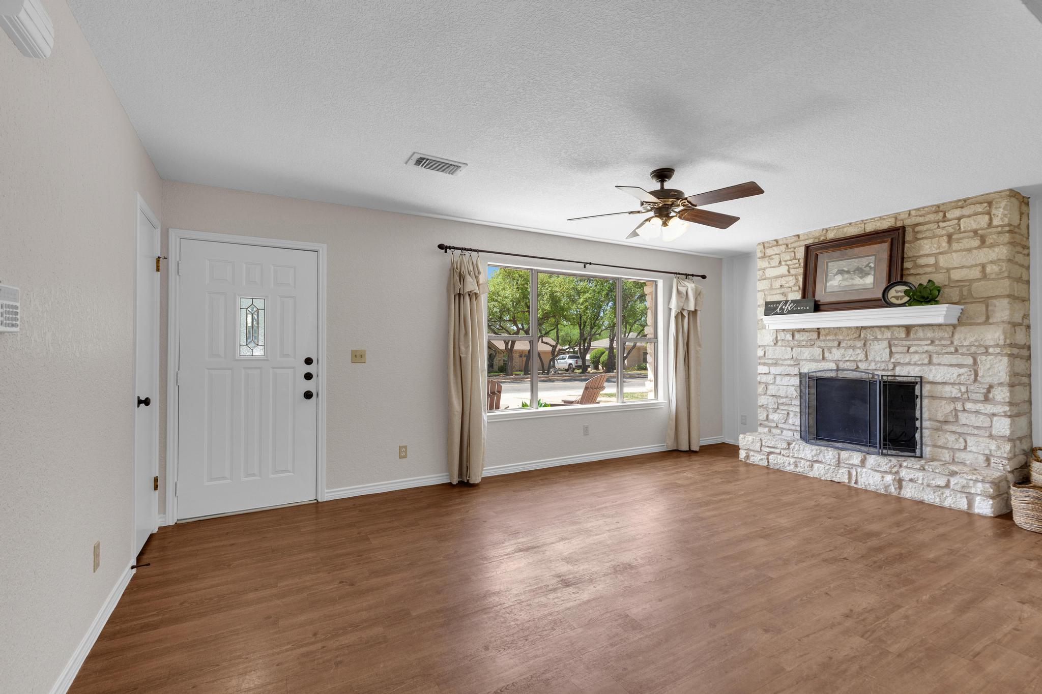7902 Bar K Ranch Road Lago Vista, TX 78645 - Photo 9 of 35 Unfurnished living room with ceiling fan, dark wood finished floors, a stone fireplace, and a textured ceiling