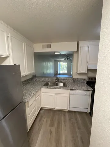 a large white kitchen with granite countertop a sink and dishwasher a stove top oven with white cabinets