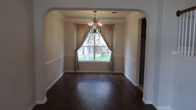 an empty room with wooden floor chandelier and windows
