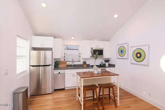 a kitchen with stainless steel appliances a refrigerator a stove a sink a dining table and chairs with wooden floor