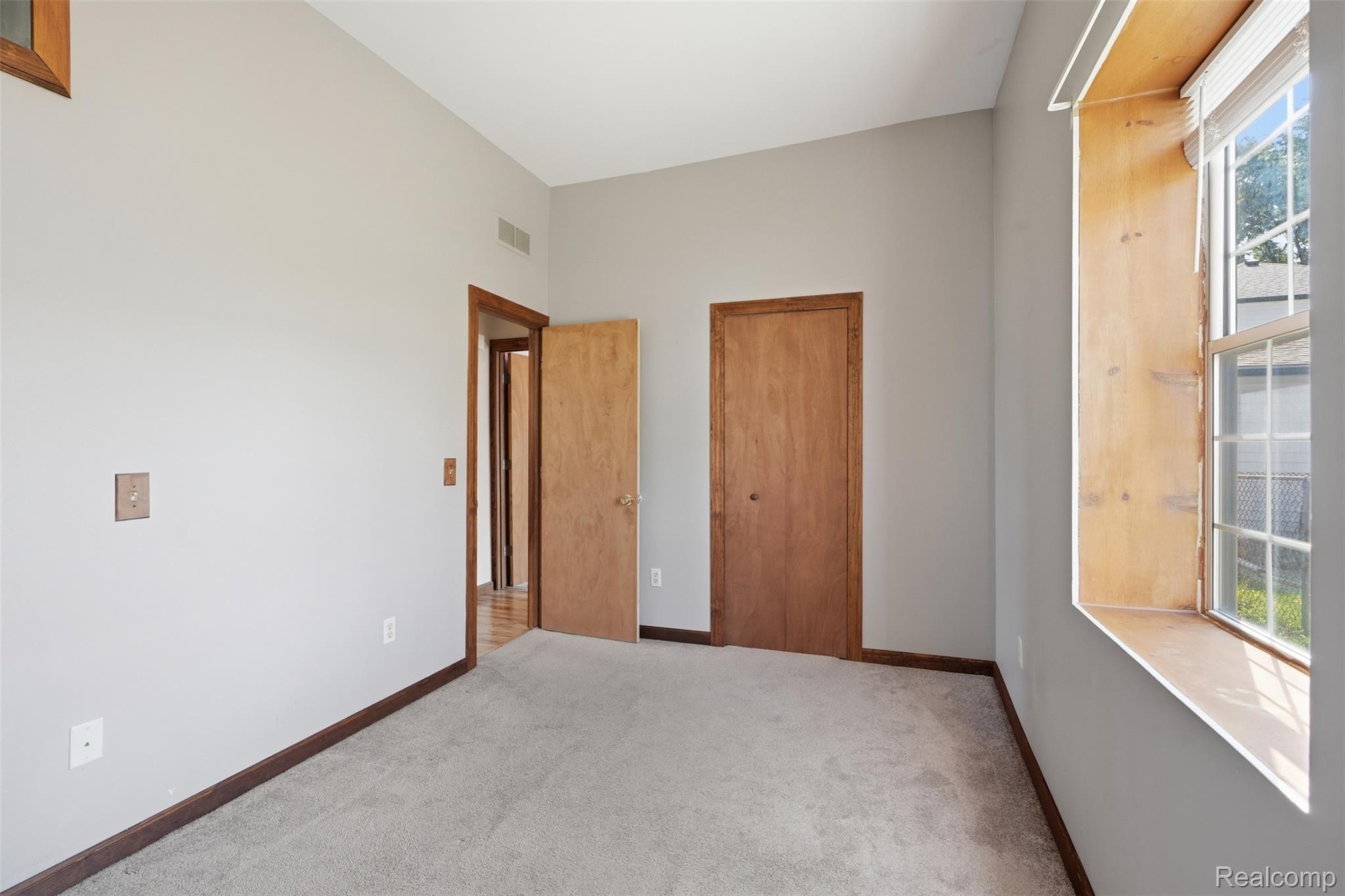 5634 Chicago Road Warren, MI 48092 - Photo 17 of 36 Carpeted room featuring a large window, light gray walls, dark wood trim, and two wood-finish doors