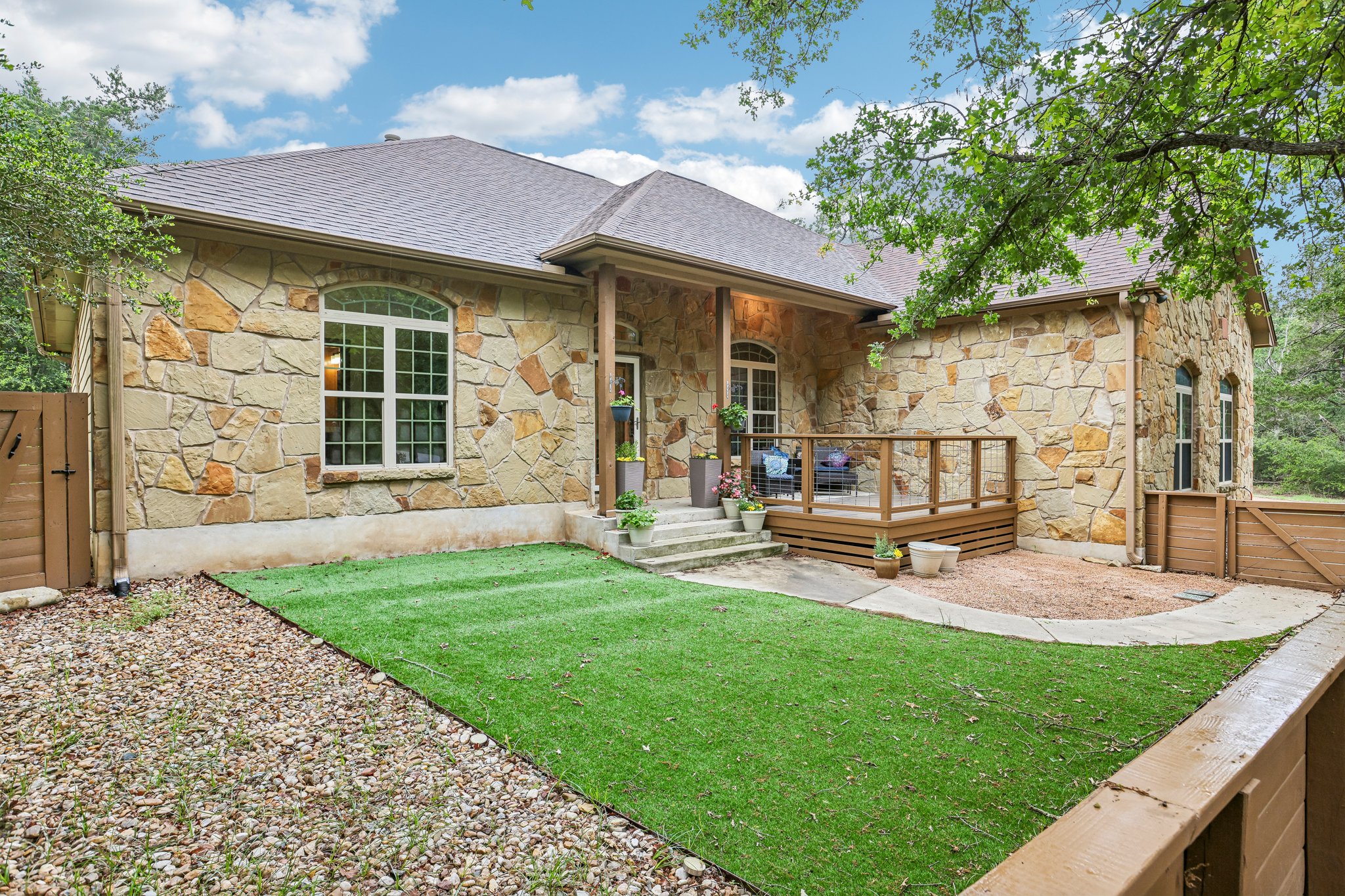Exterior featuring natural stone masonry, a covered porch with stone columns, and a wooden deck with railings