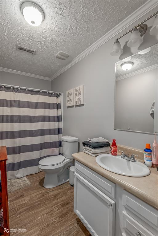 8287 Jefferson Paige Road Shreveport, LA 71119 - Photo 16 of 40 Full bath featuring a textured ceiling, vanity, ornamental molding, dark wood-style flooring, and curtained shower