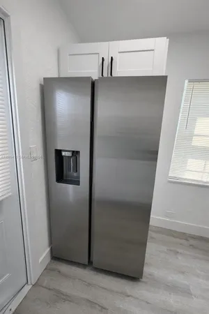 a view of a refrigerator in kitchen and an empty room with wooden floor