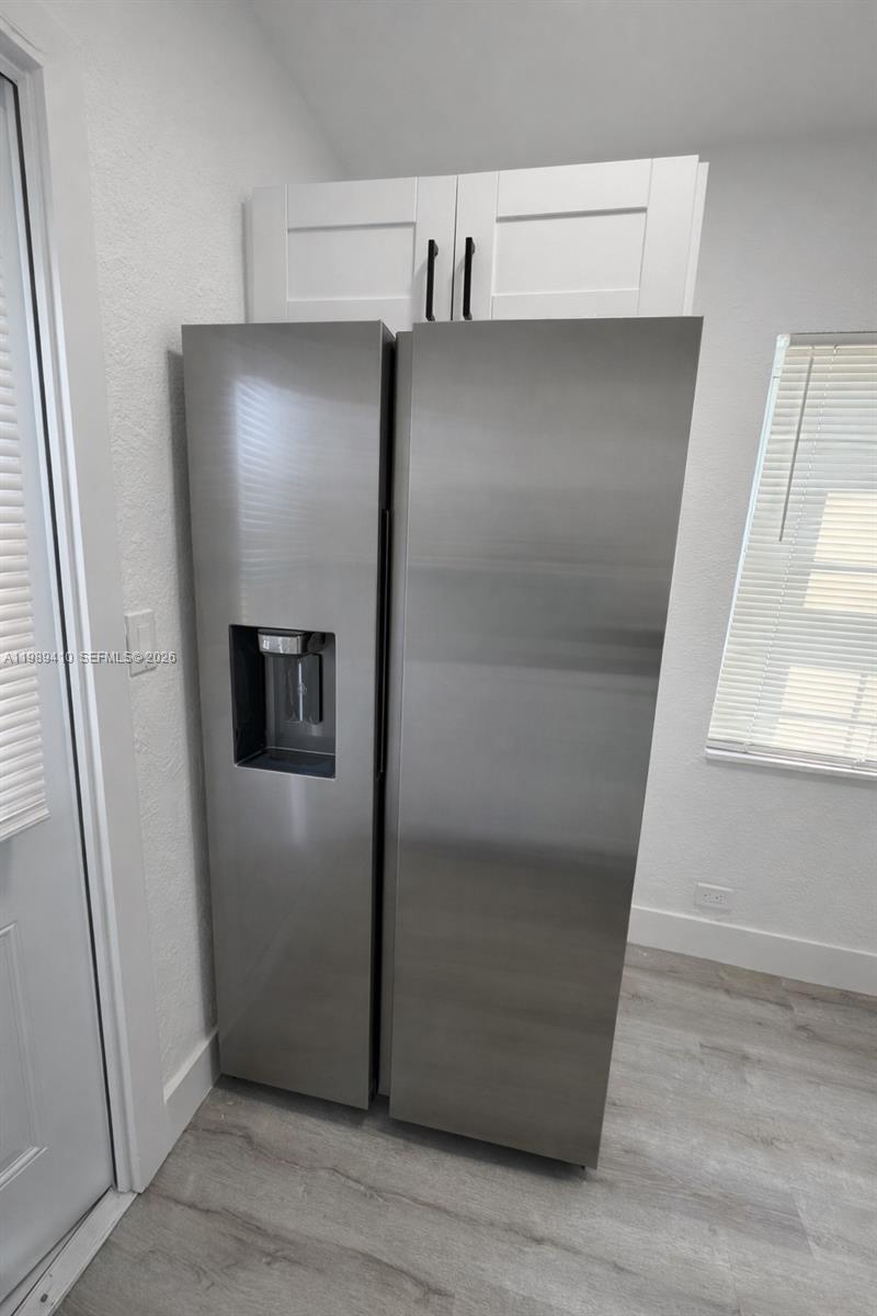 2450 Northwest 157th St Road Miami Gardens, FL 33054 - Photo 7 of 24 a view of a refrigerator in kitchen and an empty room with wooden floor