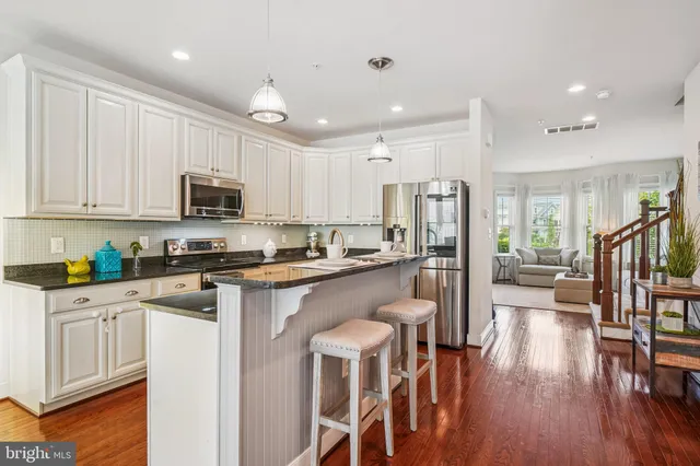 a kitchen with stainless steel appliances granite countertop a refrigerator a stove top oven a sink dishwasher and white cabinets with wooden floor