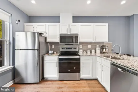 a kitchen with stainless steel appliances a stove top oven a sink a refrigerator white cabinets and wooden floor