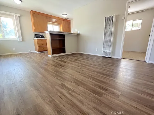 an empty room with wooden floor cabinet and windows