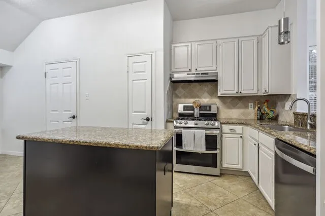 a kitchen with granite countertop a sink stainless steel appliances and white cabinets