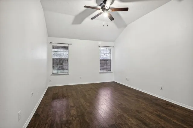 an empty room with wooden floor fan and windows