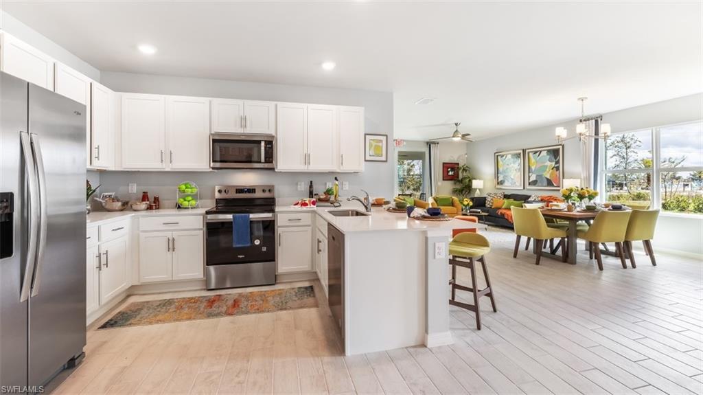 17613 Shade Tree Loop Punta Gorda, FL 33982 - Photo 4 of 27 a kitchen with stainless steel appliances granite countertop a refrigerator a stove top oven a sink dishwasher a dining table and chairs with wooden floor