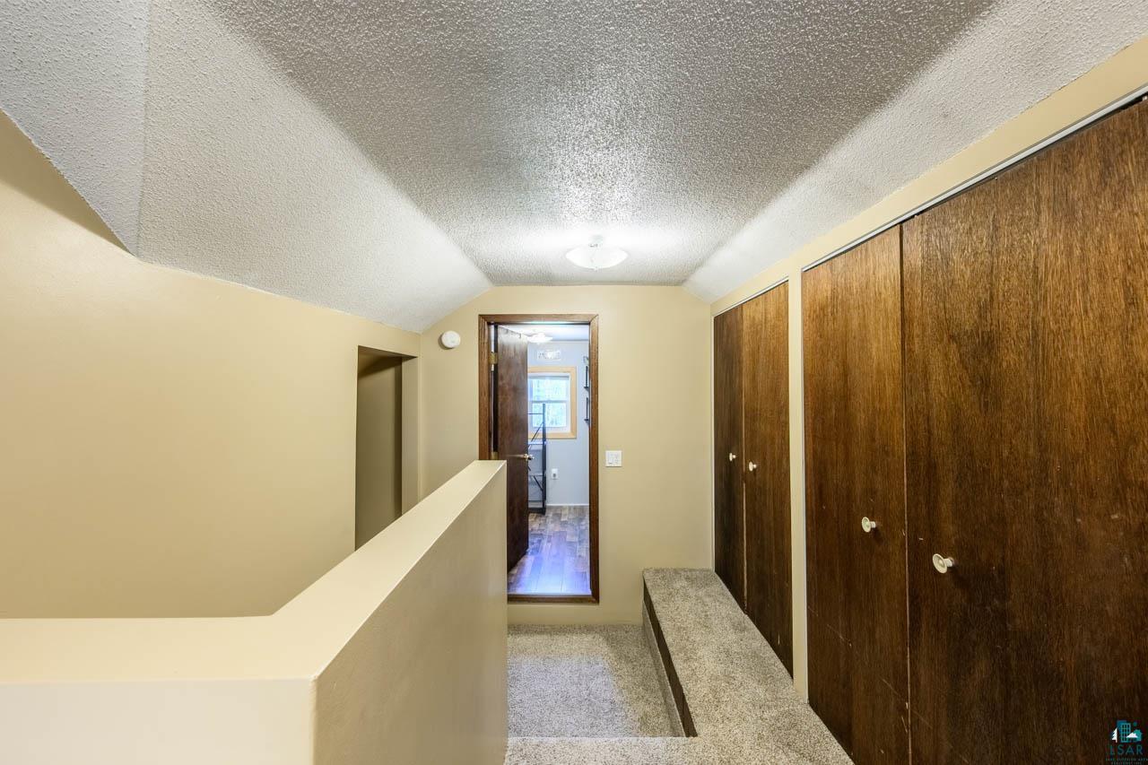 2581 O'Rourke Road Hibbing, MN 55746 - Photo 18 of 61 Hallway featuring multiple wood-finish bi-fold doors, textured ceiling, and carpeted flooring