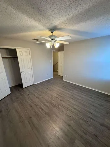 an empty room with wooden floor chandelier fan and windows