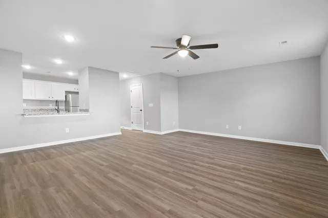 a view of an empty room with wooden floor and a kitchen